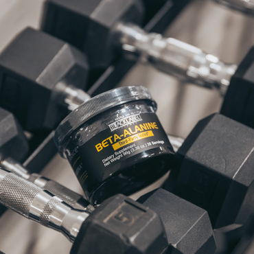 Blacklabel Beta-Alanine supplement container resting on dumbbells in a gym setting.